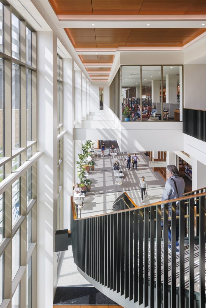Interior of Carmel Clay Public Library showing staircase, natural light and patrons in reading spaces.