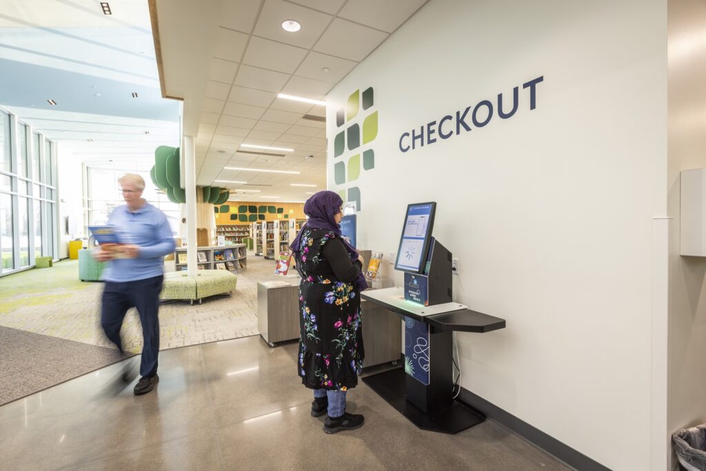 A patron using the selfCheck 3000 kiosk at Cincinnati & Hamilton County Public Library, with a modern and inviting library space in the background.