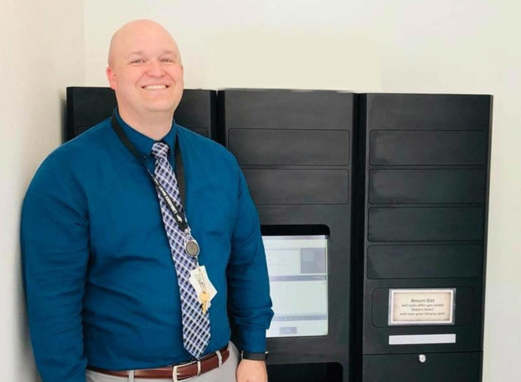 Summit County Library Director, Dan Compton, standing beside the newly installed remoteLocker during the grand opening celebration, smiling and wearing a blue shirt and tie.