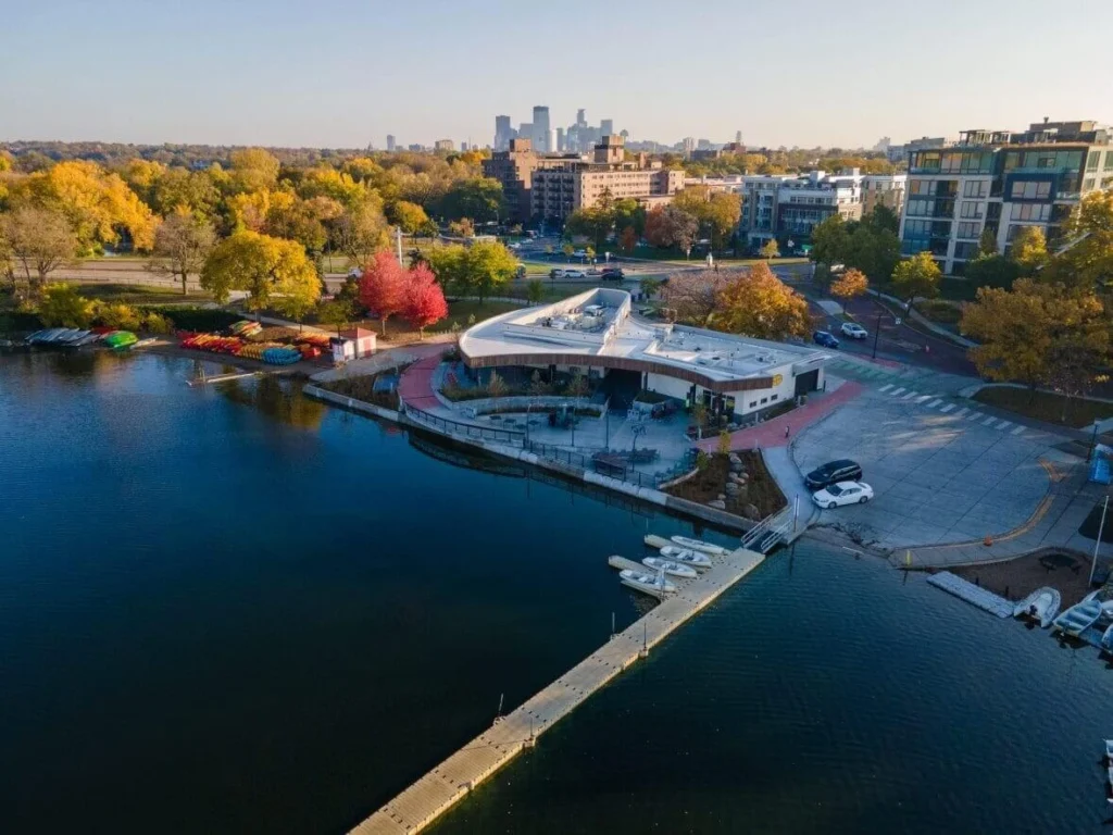 Aerial view of Bde Maka Ska Pavilion in Minneapolis surrounded by autumn colors, boats, and lakeside activity.