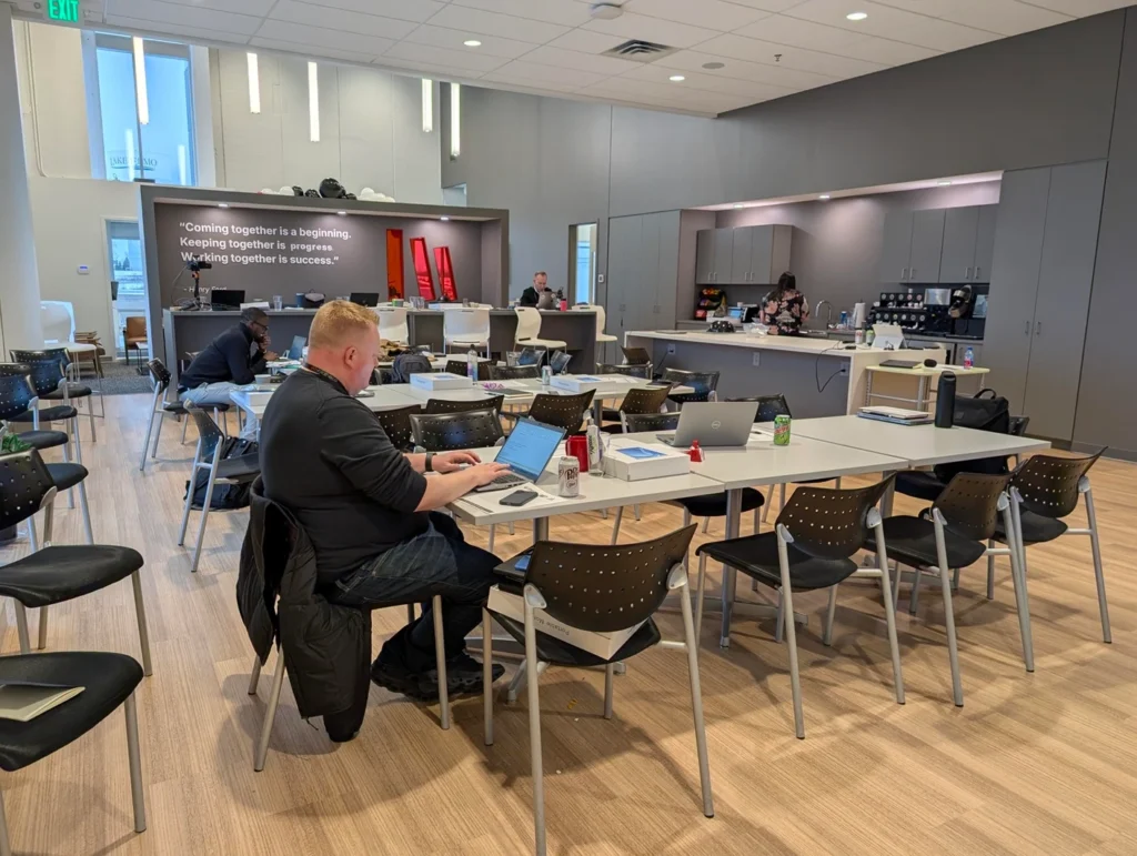 Employees working and socializing in Bibliotheca’s modern café area, with tables, chairs, and a fully equipped kitchen in the background.