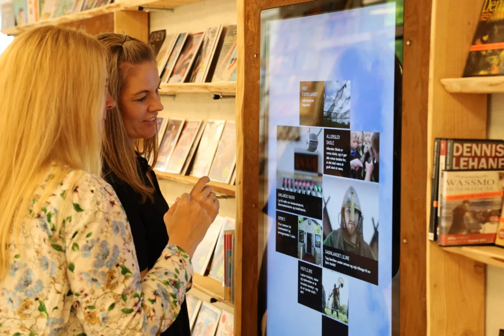 Two women interacting with a large digital screen displaying library content at a public library.